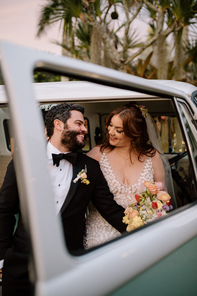 a couple looking at one another in an antique car after their ceremony at a palm tree farm